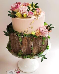 a three tiered cake decorated with flowers and greenery on a white pedestal next to a card