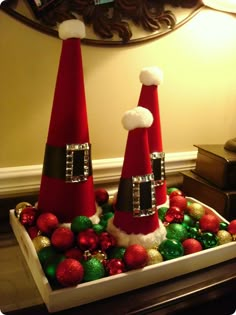 two red and black santa hats sitting on top of a tray filled with christmas ornaments