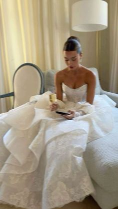 a woman in a white wedding dress sitting on a bed looking at her cell phone