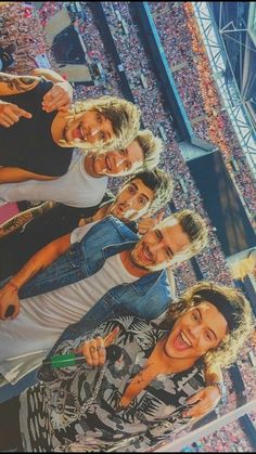 four men standing in front of a crowd at a football game with one holding a cell phone