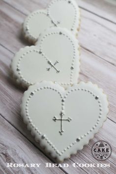 two white heart shaped cookies with crosses on them sitting on a wooden table next to each other