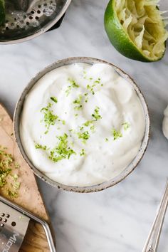 a bowl filled with sour cream next to limes on a cutting board and utensils