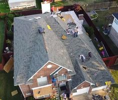 an aerial view of people working on the roof of a house in front of a yard