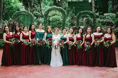 a group of women standing next to each other in front of green plants and trees