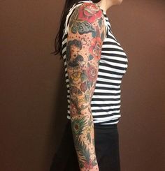 a woman with a tattoo on her arm and shoulder standing in front of a wall