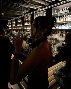 a woman sitting at a bar with a glass in her hand and bottles behind her