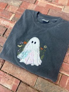 a black t - shirt with a ghost drawn on the front and back, sitting on a brick floor