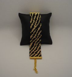 a black and gold pillow with a chain hanging from it's side on a white surface