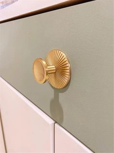 a close up of a gold knob on a green cabinet door with white drawers in the background