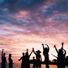 a group of people standing on top of a beach next to the ocean at sunset