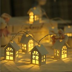 some small white houses are lit up on a table with lights in front of them