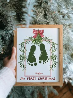 someone holding up a christmas ornament in front of a fir tree with the words my first christmas