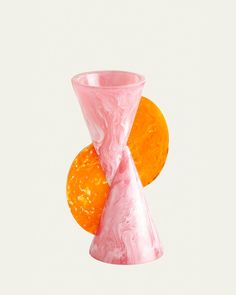 a pink and orange vase sitting on top of a white table next to an orange slice