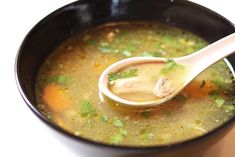 a spoon full of soup with broth and parsley on top in a black bowl