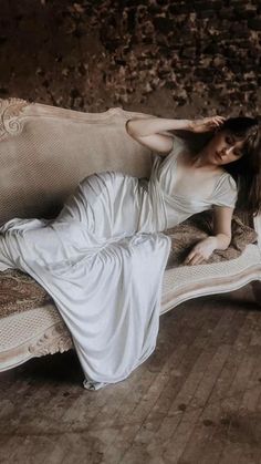 a woman laying on top of a white couch in a room with wood flooring