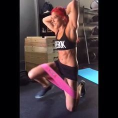 a woman with red hair and no shirt is doing exercises on a pink exercise band