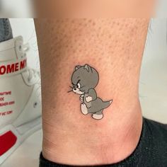 a small tattoo on the ankle of a person's leg, with an image of a cat holding a mouse