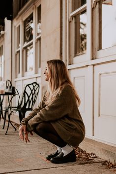 a woman sitting on the ground next to a black table and chair in front of a building