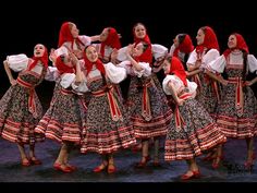 a group of women dressed in traditional polish folk costumes dancing on stage with red headscarves