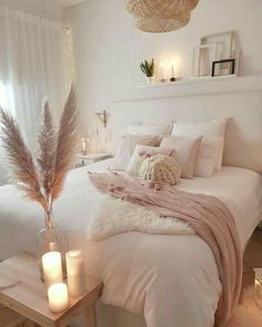 a white bed with pillows and blankets on top of it next to two lit candles