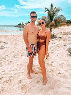 a man and woman in swimsuits standing on the beach with palm trees behind them