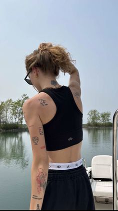 a woman with tattoos on her back standing in front of a boat looking out at the water