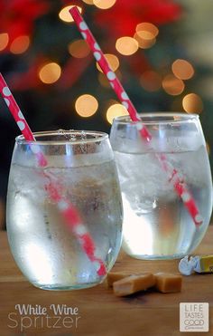 two glasses filled with water and straws on top of a wooden table next to a christmas tree