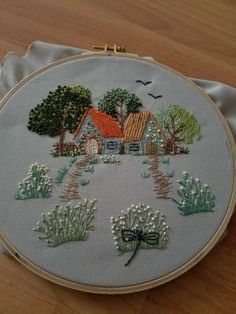 a hand embroidered house with trees and bushes on the front is sitting on a wooden surface