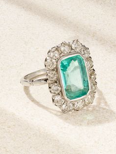 an emerald and diamond ring on a white surface