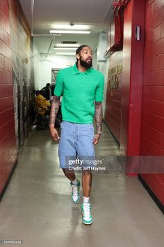 a man in green shirt and blue shorts walking down the hallway with his head tilted