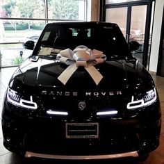 a black car with a bow on it's hood is parked in front of a large window