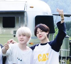 two young men standing next to each other in front of a truck and pointing at the camera