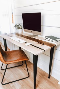 a wooden desk with a computer monitor and glasses on it next to a brown chair