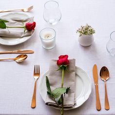 a white table topped with plates and silverware next to a vase filled with red roses