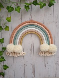 a rainbow shaped wall hanging on a white wooden wall with ivy growing up the side