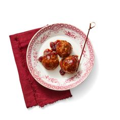 three meatballs on a white plate with a red napkin and fork next to it