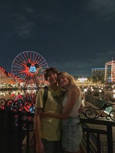 two people standing next to each other in front of a ferris wheel at night time