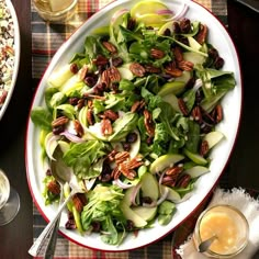 a salad with apples, pecans and nuts in a bowl next to a glass of orange juice