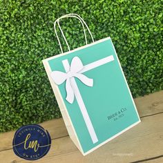 a blue gift bag with a white bow on it sitting next to a green hedge