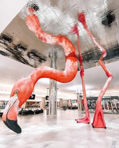 two flamingos are standing in the middle of an airport lobby, one is upside down