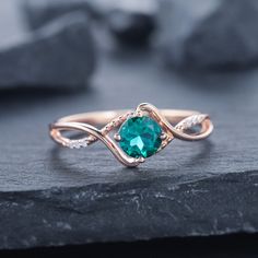 a ring with a green stone in the middle and two diamonds around it on top of a rock