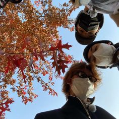 a woman wearing a face mask standing in front of a tree with leaves on it