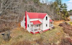 an aerial view of a white house with red roof in the middle of a wooded area