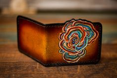 a leather wallet with a flower on the front is sitting on a wooden table,