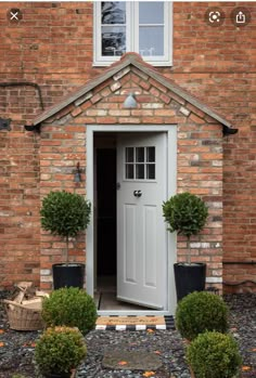 a white door with two potted plants in front of it on the side of a brick building