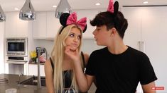 a man standing next to a woman in a kitchen wearing minnie ears on her head