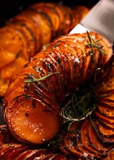 sliced up sweet potatoes on a platter with a knife and sprig of rosemary