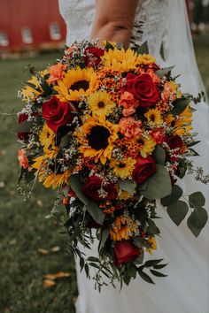 a bride holding a bouquet of sunflowers and red roses in her wedding dress