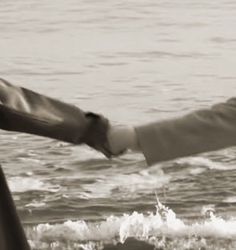 two people holding hands over the ocean waves