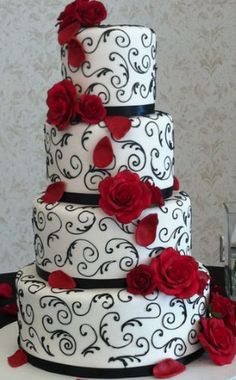 a three tiered wedding cake with red roses on the top and black swirls